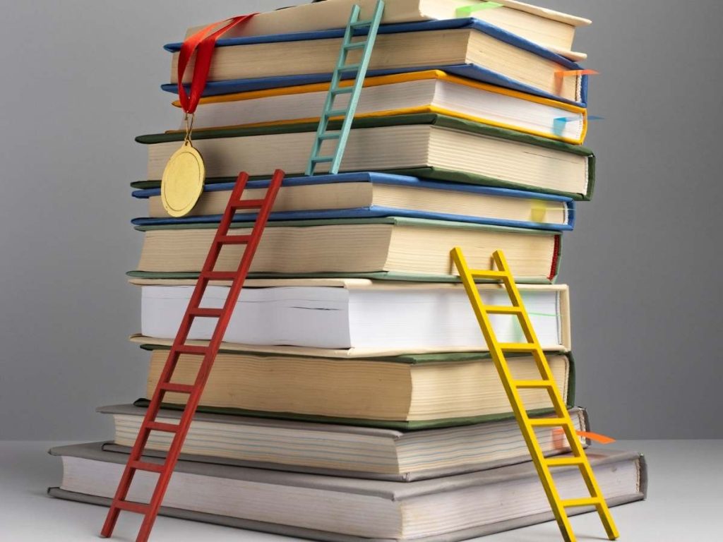 Pila di libri con scale colorate appoggiate, simbolizzando l'ascensione accademica