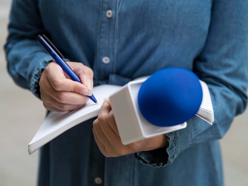 Giornalista che scrive su un bloc-notes con microfono blu